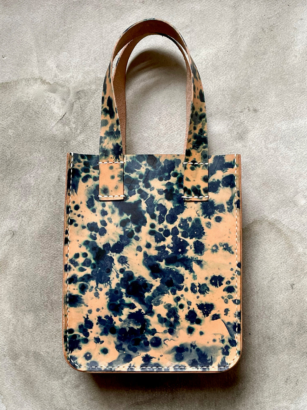An indigo-dyed natural leather tote bag with two handles and a zipper closure.
